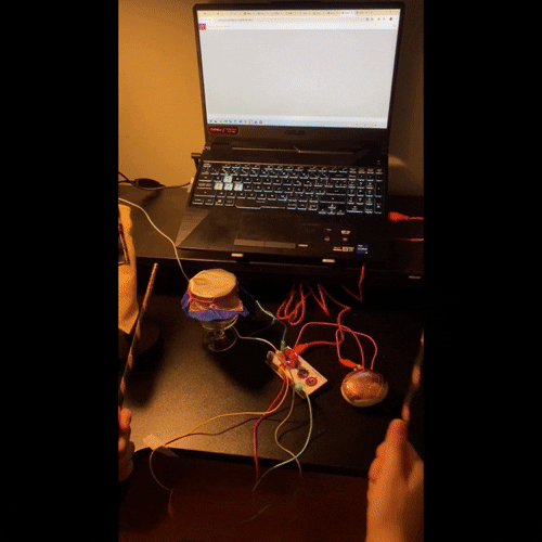 I used a variety of materials, including conductive thread, reflective and non-woven fabrics, conductive fabric and copper tape, stones, cardboard, and household items to emphasize the diversity of interactions. Each component acts as a unique drum input: chopsticks act as drumsticks, stones wrapped in copper tape act as one drum, glasses covered in multiple layers of fabric act as another, my table lamp becomes the third drum, and cardboard pedals complete the setup along with a foot switch.